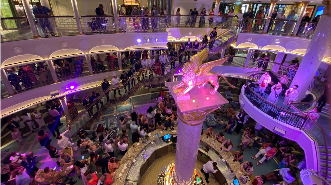 The cruise director speaks to guests in the Carnival Venezia's atrium to recognize the ship's officers.
